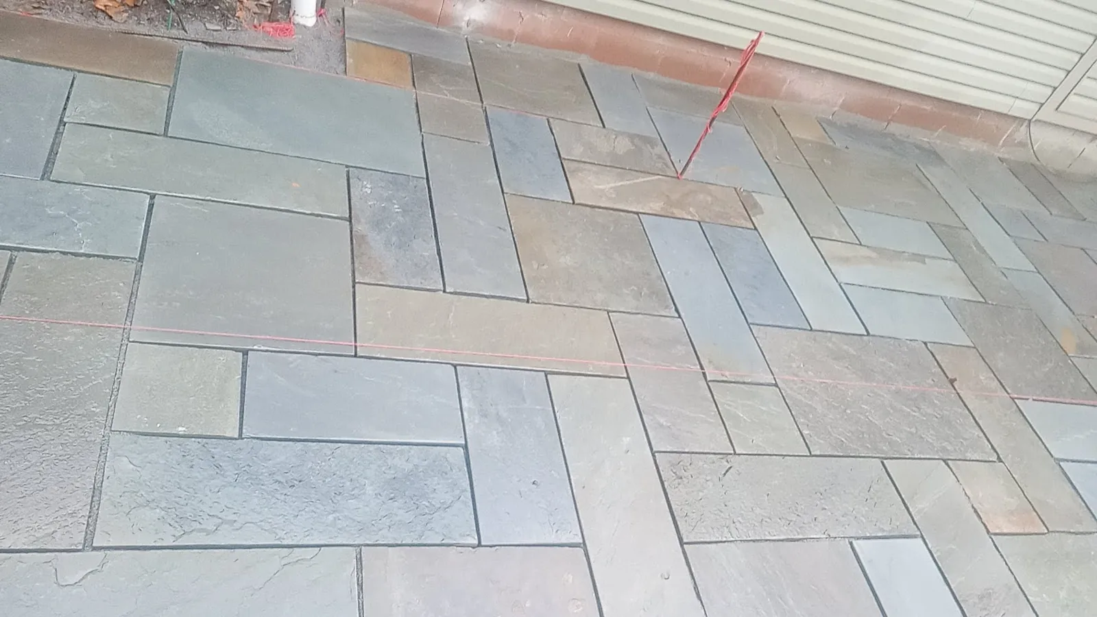 Bluestone patio being laid in a pattern beside a house