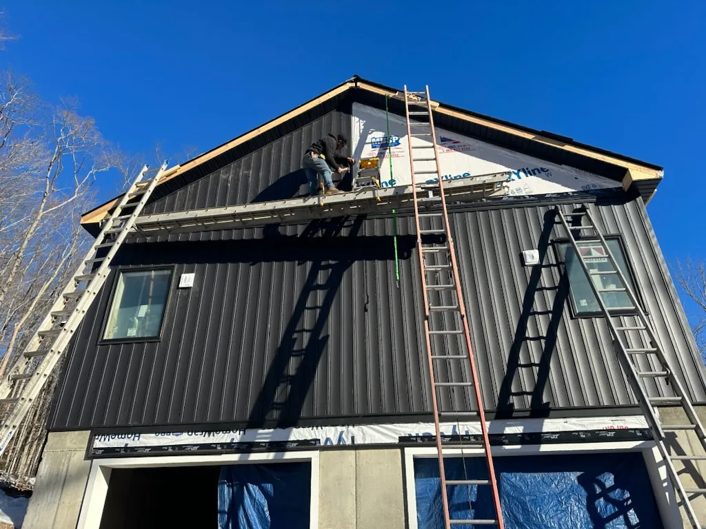 Crew installing dark metal siding on a gable